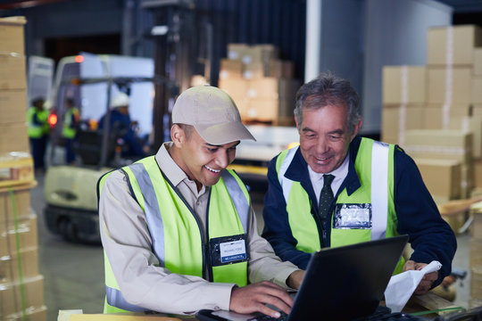 Manager and worker using laptop at distribution warehouse loading dock
