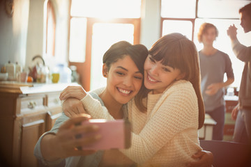 Young women friends taking selfie with camera phone in apartment