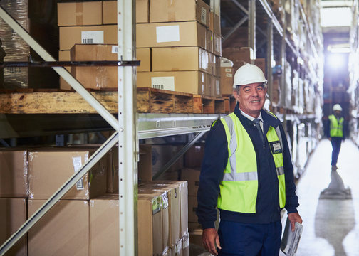 Portrait smiling manager with clipboard next to shelf in distribution warehouse