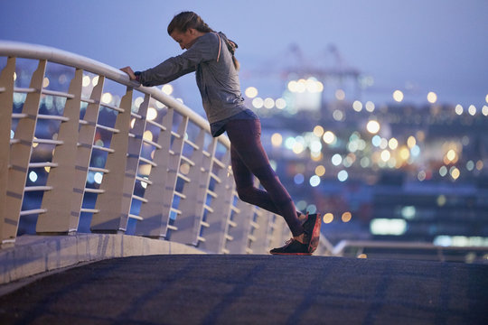 Female runner stretching legs on urban footbridge at dawn