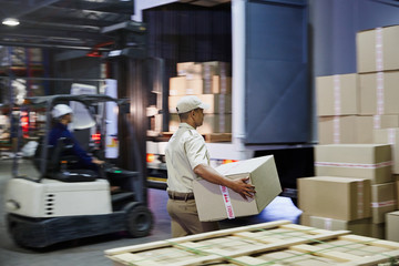 Workers and forklift loading cardboard boxes onto trucks at distribution warehouse loading dock