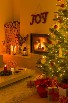 Ambient fireplace and candles illuminating living room with Christmas tree and decorations