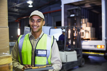 Portrait smiling worker in front of forklift and truck at distribution warehouse loading dock