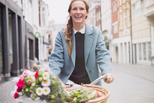 Smiling woman riding bicycle with flowers in basket