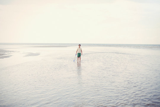 Portrait boy holding shove in ocean surf on overcast summer beach
