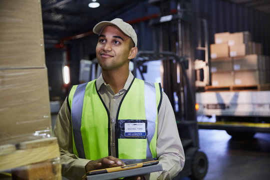 Worker with clipboard checking boxes in distribution warehouse