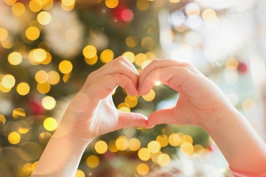 Close up hands of girl forming heart-shape in front of Christmas tree