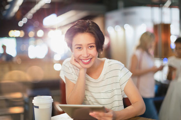 Portrait smiling young woman using digital tablet and drinking coffee in cafe