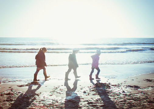 Brother and sisters in warm clothing walking in wet sand on sunny beach