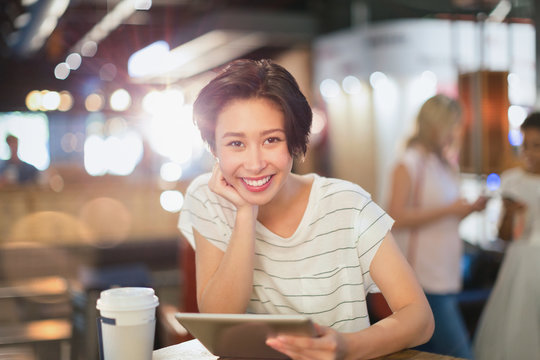 Portrait smiling young woman using digital tablet and drinking coffee in cafe