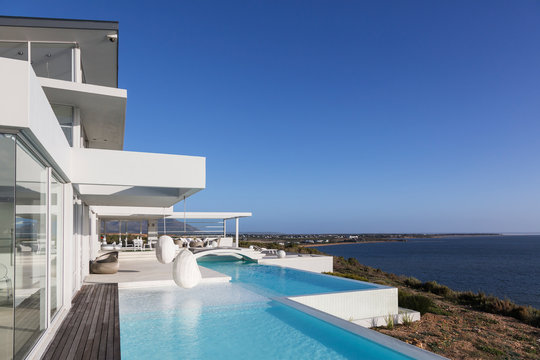 Sunny, tranquil modern luxury home showcase exterior with infinity pool and ocean view under blue sky