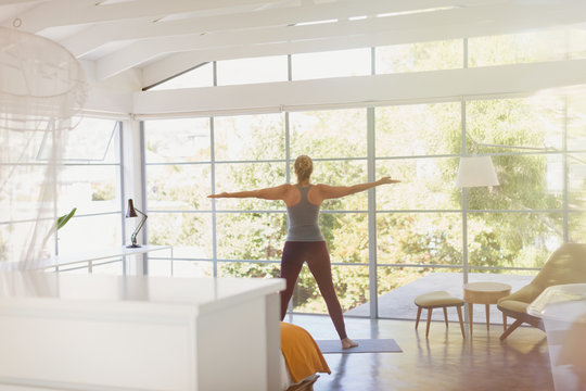 Woman practicing yoga with arms outstretched in sunny modern bedroom