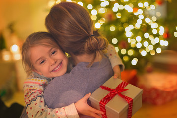 Smiling daughter with Christmas gift hugging mother