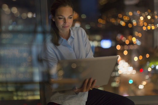 Serious businesswoman working late at laptop in office window at night