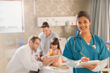 Portrait confident female nurse taking notes on medical record while doctor shows digital tablet to girl patient in hospital