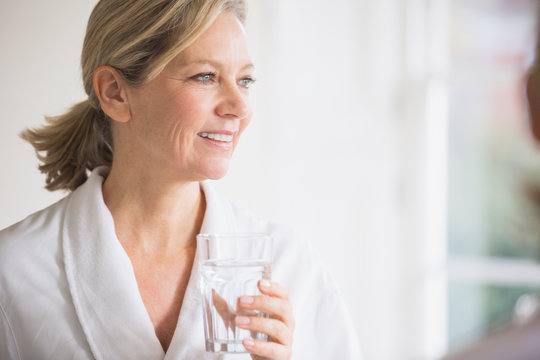 Smiling mature woman in bathrobe drinking water