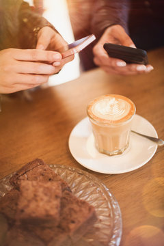 Women with camera phones photographing cappuccino design at cafe table