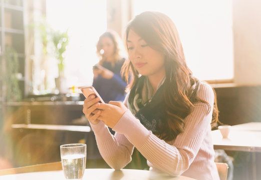 Woman texting with cell phone at cafe table