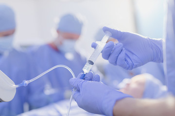 Close up anesthesiologist with syringe injecting anesthesia medicine into IV drip in operating room