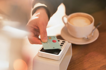Close up man paying for cappuccino with credit card contactless payment in cafe