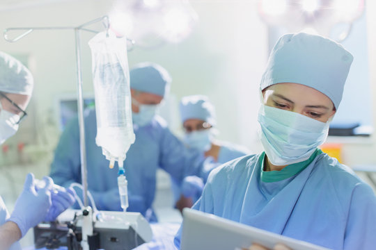 Female surgeon wearing surgical mask using digital tablet in operating room