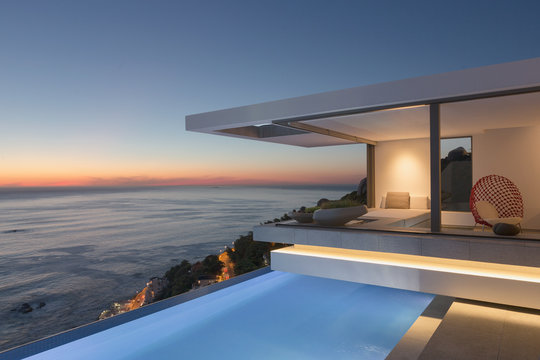 Illuminated modern, luxury home showcase exterior patio with lap pool and ocean view at twilight