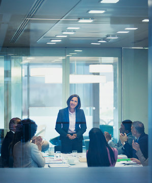 Colleagues clapping for businesswoman leading conference room meeting