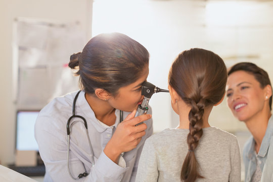 Female pediatrician using otoscope, checking ear of girl patient in examination room