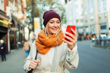 Young woman with headphones and smart phone video chatting on autumn street