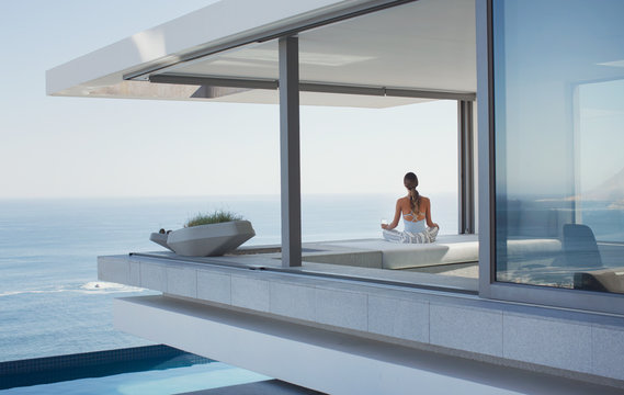 Serene woman meditating on modern, luxury home showcase exterior patio with ocean view