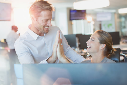 Businessman and businesswoman high-fiving at computer in office