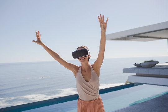 Energetic woman using virtual reality simulator glasses on modern, luxury home showcase exterior patio with ocean view