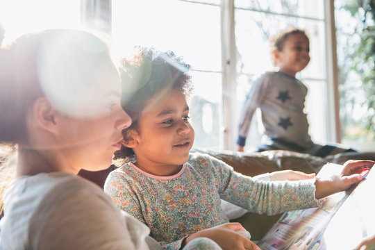 Mother and daughter reading book in sunny living room