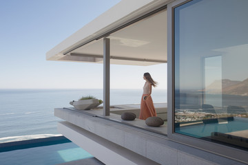 Woman looking at ocean view on modern, luxury home showcase exterior balcony