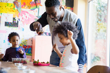 Father pouring syrup and waffles for excited toddler daughter