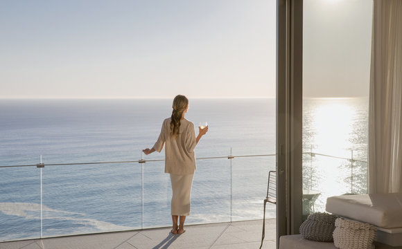 Woman standing on sunny luxury balcony with ocean view