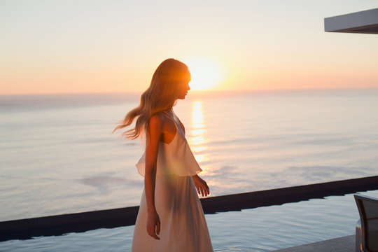 Woman in white dress on tranquil luxury patio with sunset ocean view