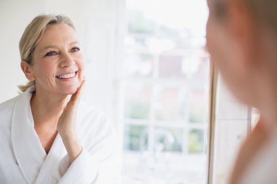 Smiling mature woman touching face at bathroom mirror