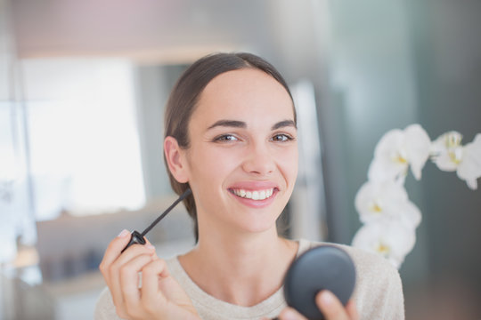 Portrait smiling, confident woman applying mascara with mascara wand and compact mirror