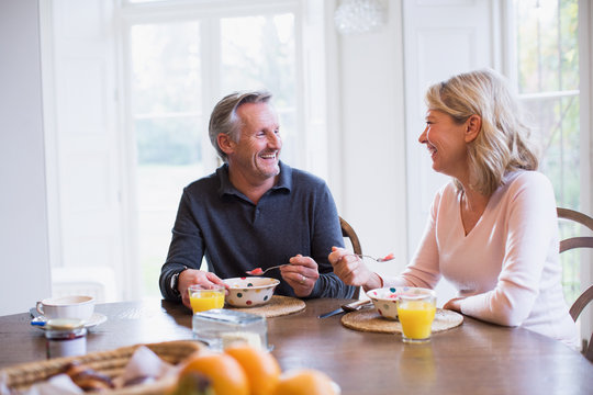 Smiling mature couple eating breakfast and talking at dining table