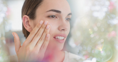 Brunette woman applying face moisturizer to cheek