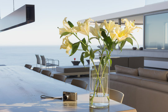 Yellow lily bouquet in vase on modern, luxury home showcase interior dining table next to digital camera