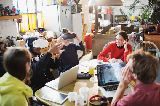 Young college student friends studying, using virtual reality simulator glasses at kitchen table in apartment