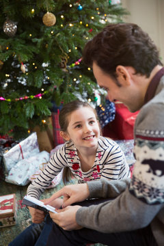 Father reading book with daughter at Christmas tree