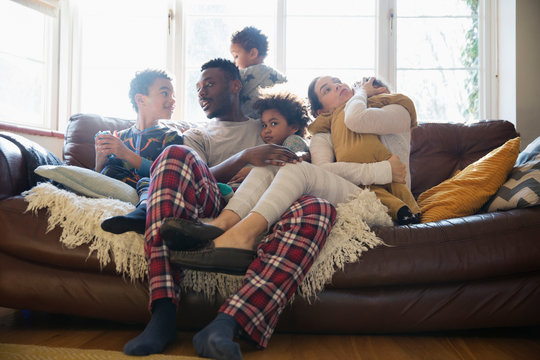Young Family Relaxing In Pajamas On Living Room Sofa