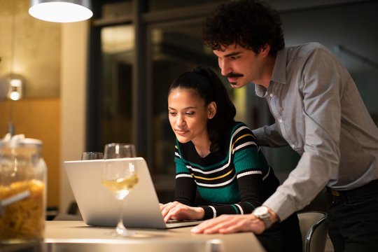 Couple Using Laptop And Drinking White Wine At Home At Night