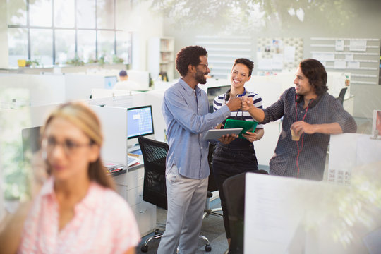 Excited creative business people fist bumping, celebrating in office