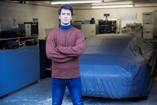 Portrait confident man standing in front of covered car in garage
