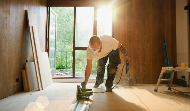 Construction worker using electric saw to cut wood in house