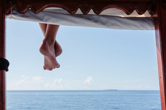 Bare feet hanging from dock over sunny ocean, Maldives